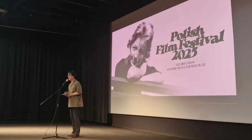 mężczyzna na scenie przemawia przed ekranem filmowym na którym wyświetlony jest tytuł festiwalu