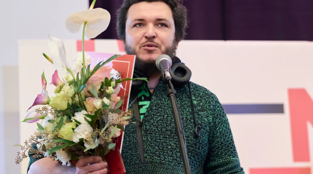 mężczyzna z kwiatami przemawia na scenie po otrzymaniu nagrody