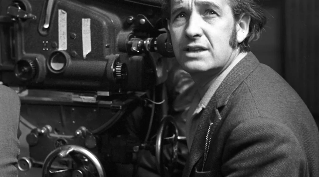 Czarno-białe zdjęcie z planu filmu „Krajobraz po bitwie”. Mężczyzna w tweedowej marynarce stoi przy dużej kamerze filmowej Arriflex i patrzy w górę, w dłoni trzyma papierosa.