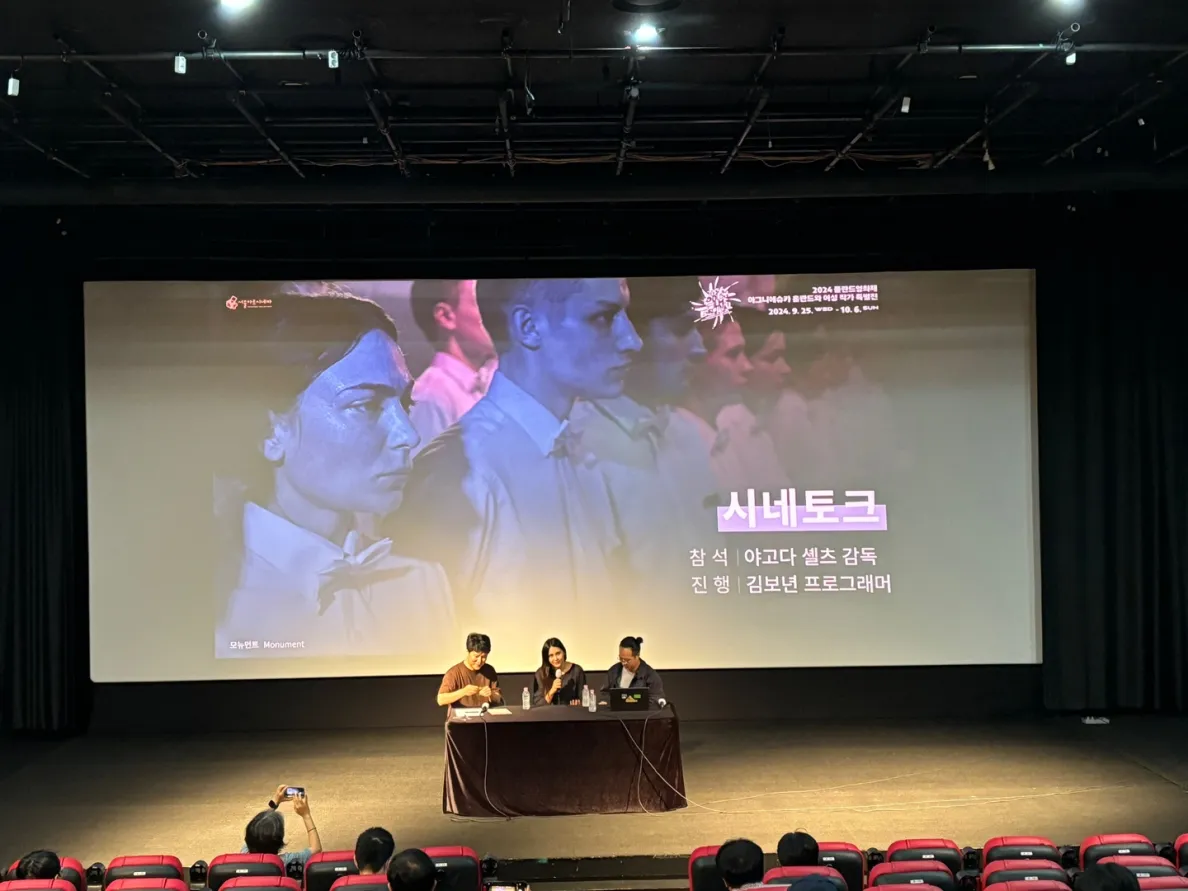 pokaz filmowy w kinie, widoczne podium z prelegentami z a którymi jest ekran z koreańskimi napisami