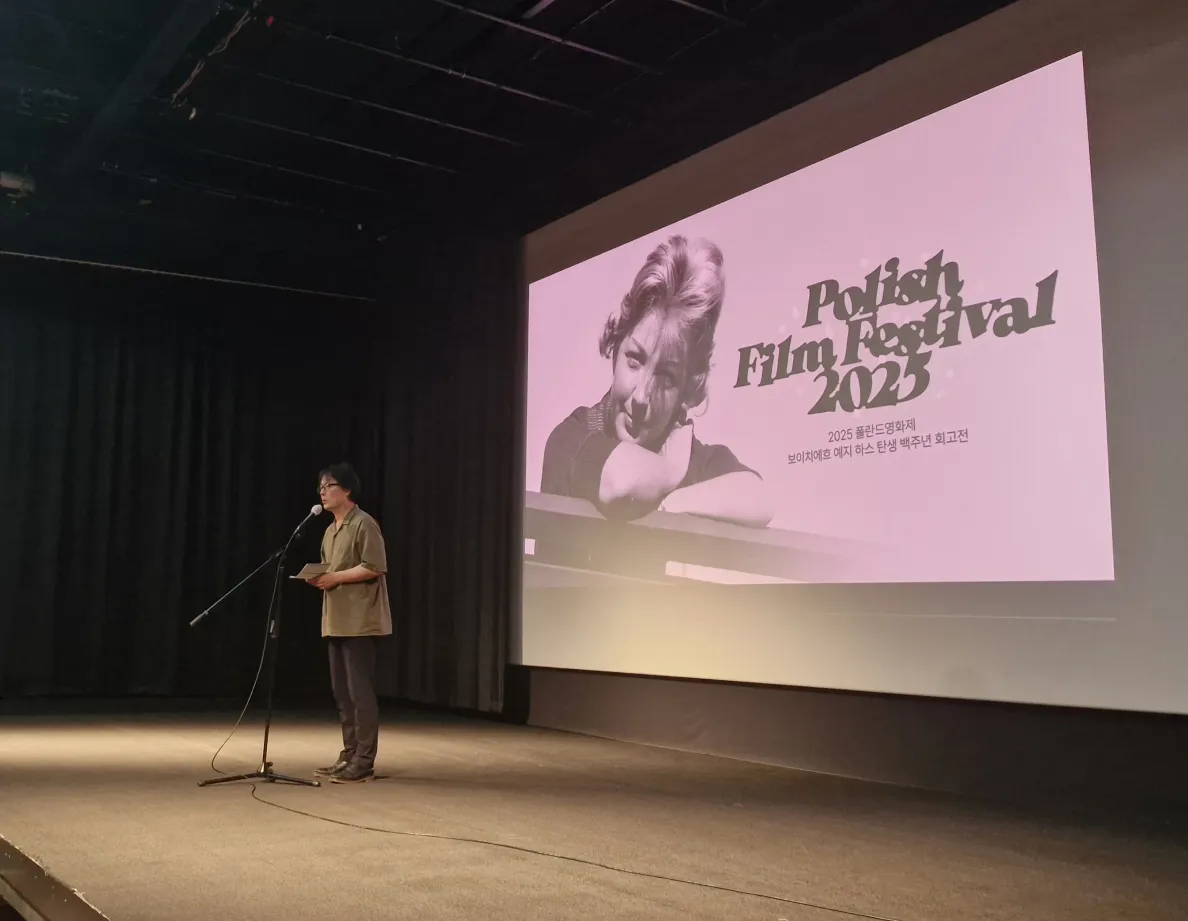 mężczyzna na scenie przemawia przed ekranem filmowym na którym wyświetlony jest tytuł festiwalu