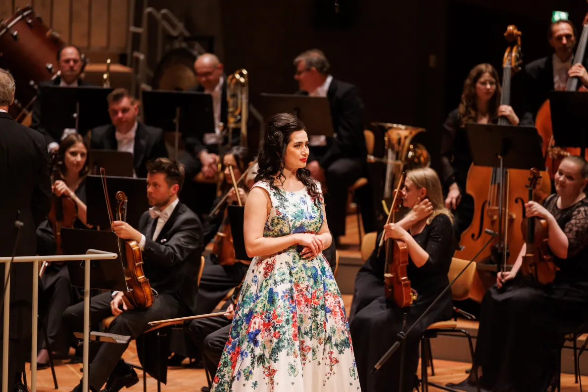 kobieta w kwieciszej sukni wraz z klasycznymi muzykami na scenie