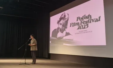 mężczyzna na scenie przemawia przed ekranem filmowym na którym wyświetlony jest tytuł festiwalu