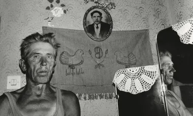 starszy, szczupły mężczyzna stoi w swoim mieszkaniu