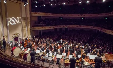 na pierwszym planie orkiestra na scenie, w tle widoczna zgromadzona publiczność