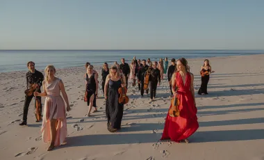 członkowie orkiestry w koncertowych strojach na plaży