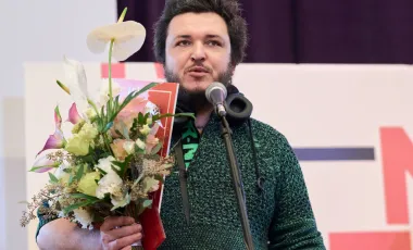 mężczyzna z kwiatami przemawia na scenie po otrzymaniu nagrody