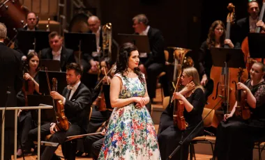 kobieta w kwieciszej sukni wraz z klasycznymi muzykami na scenie