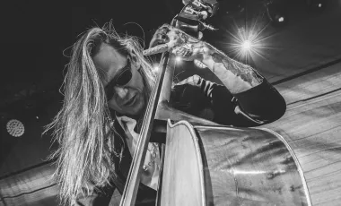 zdjęcie Wojciecha Mazowewskiego grającego w ciemnych okularach na basie