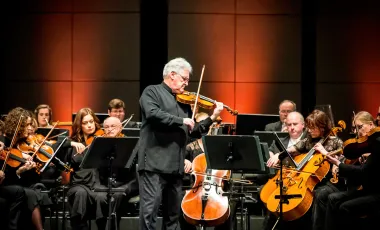 mężczyzna stojąc gra na skrzypcach, prowadzi orkiestrę
