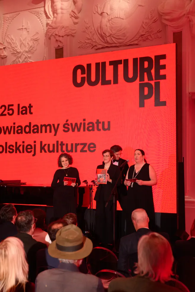 Cztery osoby na scenie przed czerwonym ekranem z napisem „Od 25 lat opowiadamy światu o polskiej kulturze”. Jedna z nich pokazuje publiczności Rocznik Culture.pl.