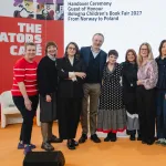 Ludzie stojący w rzędzie pod napisem "Ceremonia przekazania tytułu Gościa Honorowego BCBF 2027, Norwegia Polsce"" 