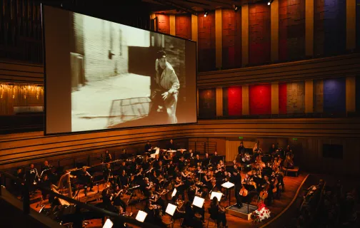 Sala koncertowa, grająca orkiestra i ekran z wyświetlonym kadrem z filmu Wajdy